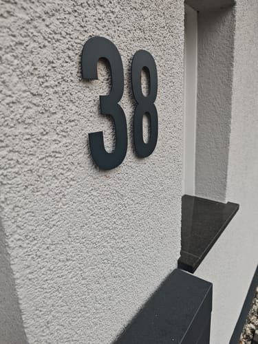 Customer's Gewagte Hausnummer, a modern black number 38 mounted on a textured light wall.