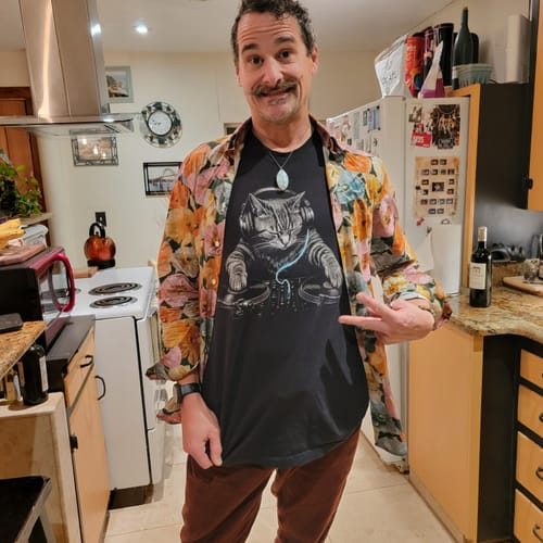 Customer's Scratch Premium black t-shirt featuring a cat DJ graphic, worn under an open floral shirt.
