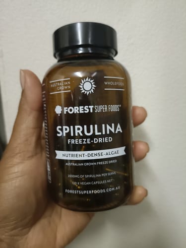 A customer's hand holding a brown bottle of Australian Freeze Dried Spirulina.