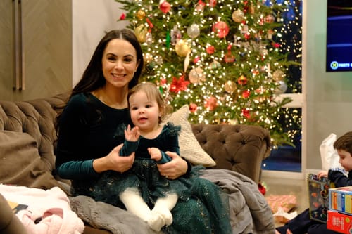 Reviewer and a child wearing matching green Velour Ballerina Dresses while sitting on a couch in front of a Christmas tree.