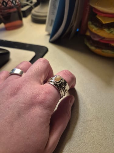 Customer wearing the wide Peach Moonstone Fidget Ring, showing its dusty rose stone on their thumb.