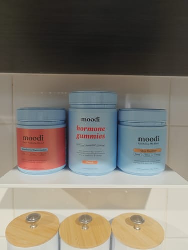 Reviewer's light blue bottle of Peach Hormone Gummies is on a white shelf between two other moodi supplement jars.
