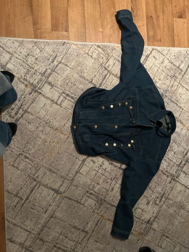 Customer's dark blue denim jacket with metal studs laid out flat on a patterned rug.