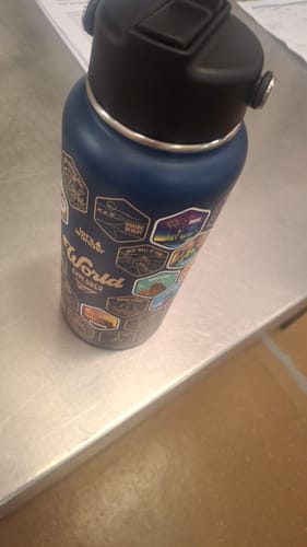 Customer's blue World Explorer Bottle with many destination stickers applied, sitting on a steel countertop.