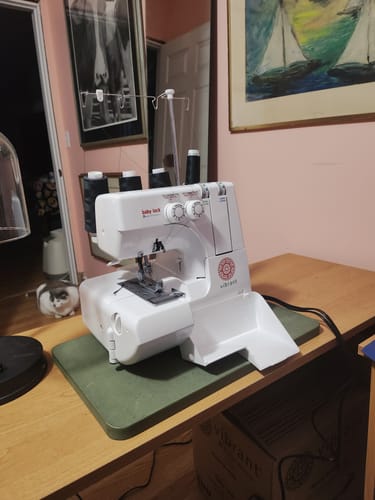 Customer's white Baby Lock Vibrant Serger set up on a wooden desk with a green mat underneath.