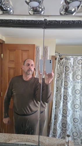 Reviewer taking a mirror selfie while wearing the brown Glacier Long Sleeve Crew base layer in a bathroom.