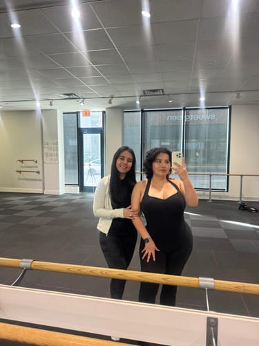 Reviewer taking a mirror selfie in a workout studio wearing the flattering black Sculpt Onesie.
