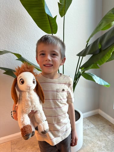 A customer's smiling child holding the fluffy Tali Plushie indoors.