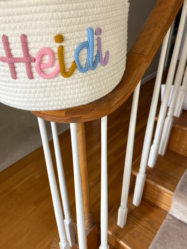 Close-up of a customer's white Personalized Knitted Basket with the name 'Heidi' in colorful yarn, sitting on a banister.