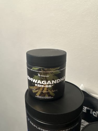 Reviewer's black jar of Ashwagandha KSM-66 supplements sitting on another product container against a plain wall.