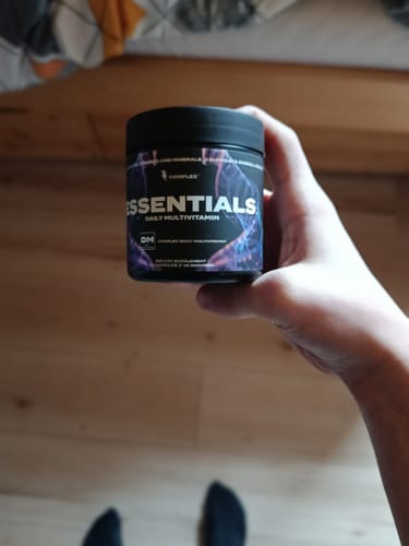 Customer holding a black tub of Essentials Daily Multivitamin in their hand.