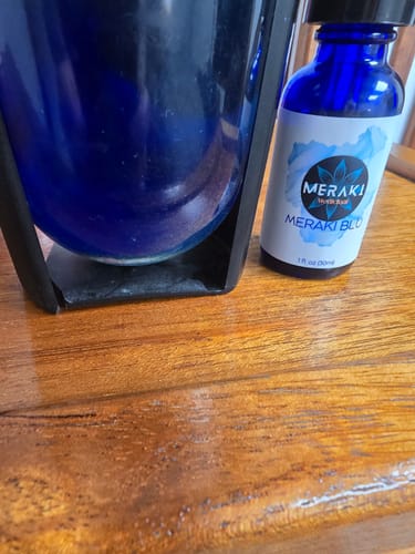 Customer's blue bottle of Meraki Blu on a wooden table.