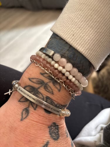 Close-up of a reviewer wearing the engraved 'Be Anxious For Nothing' bracelet on their tattooed wrist, stacked with other bracelets.