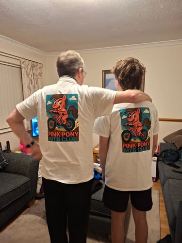 Customer showing the back of two white unisex t-shirts with a 'Pink Pony MTB Club' graphic.