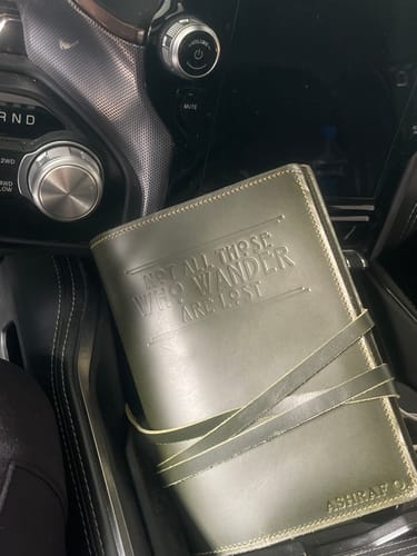 Reviewer's embossed green leather journal with a strap closure, sitting inside a car.