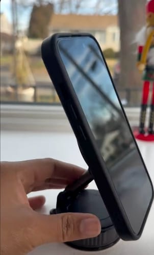 Customer's hand on the black 360° MagPro Magnetic Phone Holder, which is holding a phone on a windowsill.