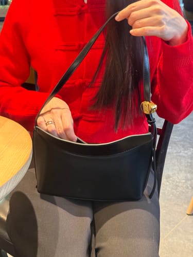 Customer in a red top holding the black Faux Leather Shoulder Bag open and reaching inside.