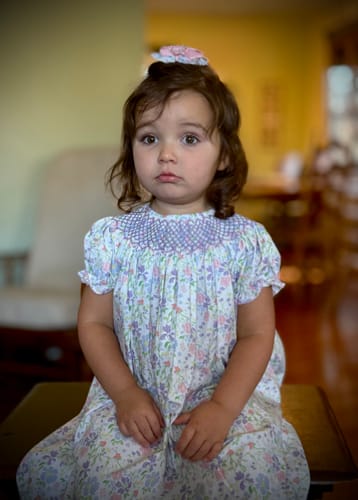 Customer's Poppy Floral Smocked Bishop Dress worn by a young child sitting indoors.
