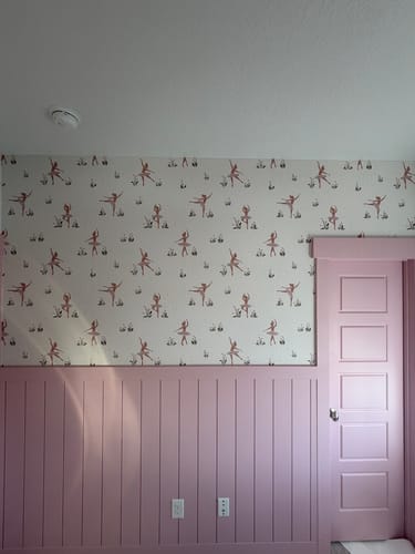 Customer's room showing the Allegra Wallpaper with a ballerina print installed above pink wainscoting.