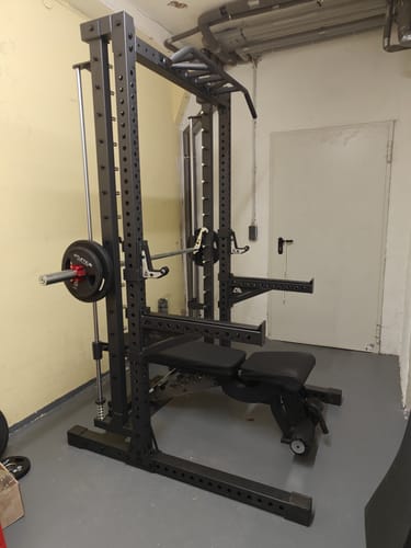 Ein Kunde zeigt das aufgebaute R7 Saber Squat Rack mit Hantelbank und Multipresse in einem Trainingsraum.