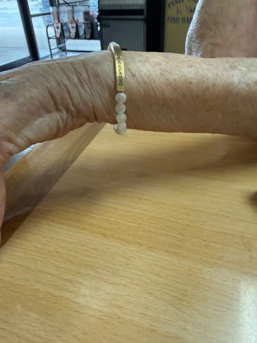 Reviewer wearing the DAUGHTER OF THE KING bracelet with light-colored beads on their arm, which is resting on a wooden table.