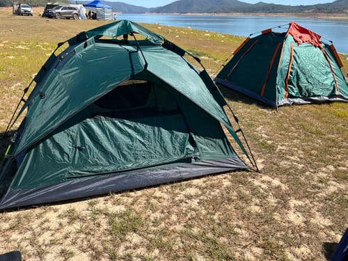Customer's green 3 Secs Tent set up on a grassy bank next to a lake, with a second tent in the background.