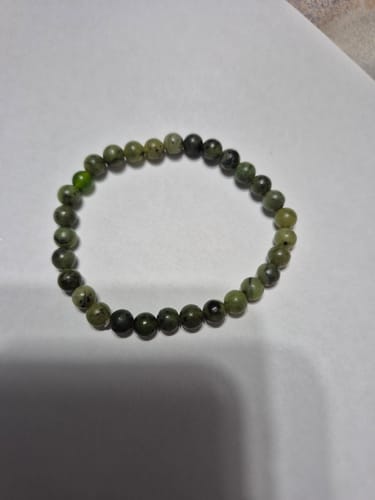 Photo d'un client montrant le bracelet Jade composé de perles vertes, posé sur une surface blanche.