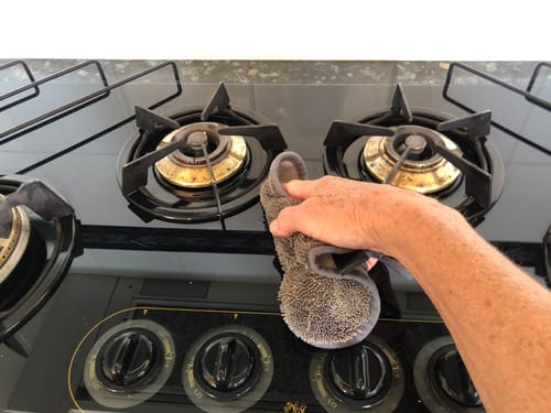Customer using the grey KoalaCloth Mini to wipe a black glass gas cooktop.