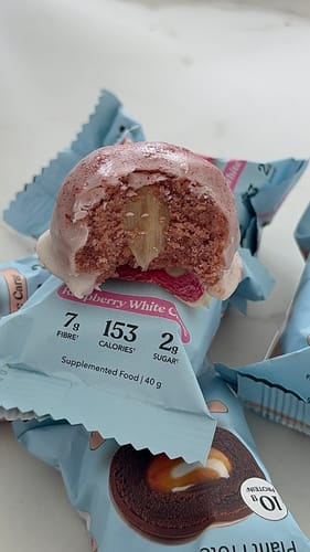 Reviewer's close-up of a bitten Raspberry White Choc Plant Protein Ball, showing the gooey center and its wrapper.
