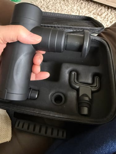 Reviewer holding the black Vibit Gun GO over its open carrying case with an attachment visible inside.