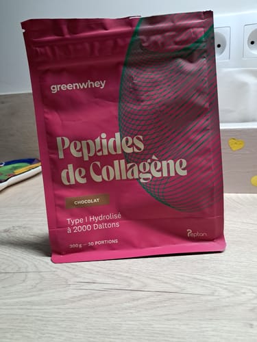 Un client montre le sachet rose de Peptides de Collagène saveur chocolat posé sur une table en bois.