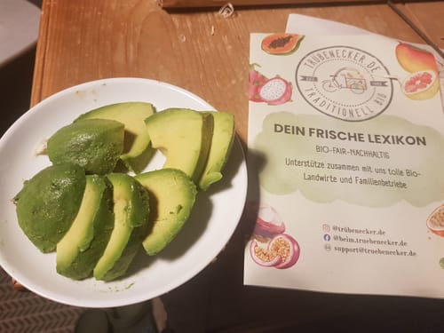 Kunde zeigt aufgeschnittene, cremige Reed & Hass Avocados in einer weißen Schüssel auf einem Tisch.