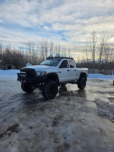 Customer's lifted white Dodge Ram with the Long Arm Upgrade Kit installed, parked on an icy surface in a snowy area.