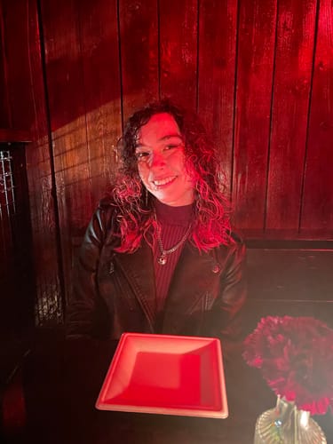 Reviewer smiling in a red-lit room, wearing the silver EVIL EYE PENDANT on a chain.