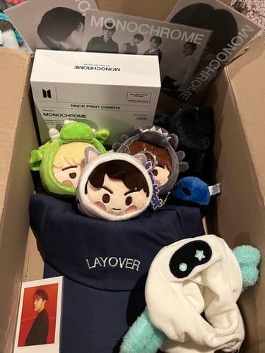 Customer's K-POP Random Box filled with BTS merch, including a print camera, plushies, and a Layover hat.