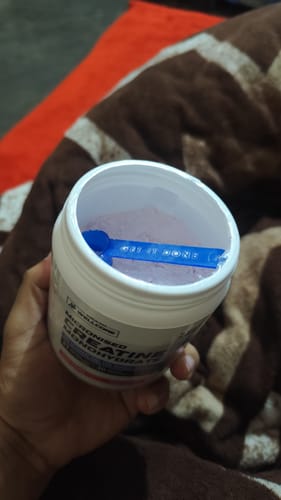 Close-up of a customer holding an open tub of Wellcore Creatine, showing the pink powder and a blue scoop inside.