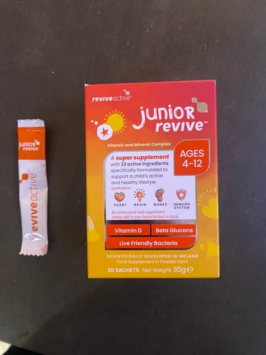 Reviewer's red and orange box of Junior Revive with a single-dose sachet shown beside it on a flat surface.