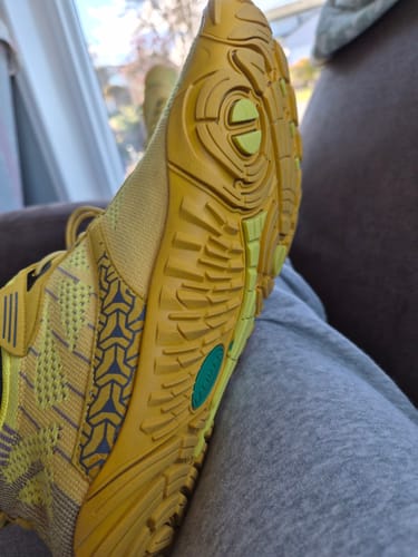 Close-up of the reviewer's yellow Free I - Barefoot Shoe, showing the textured sole and side of the shoe while resting.