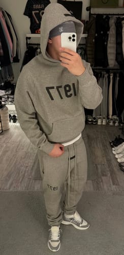 Klant in een oversized grijs Fear of God Essentials trainingspak die een spiegelselfie maakt.