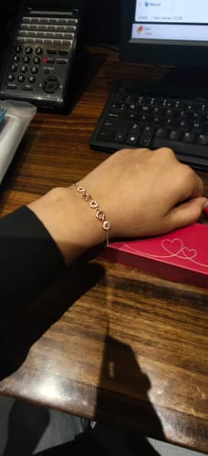 Customer wearing the Rose Gold Loving Heart Bracelet on their wrist, with the pink product box on the desk.