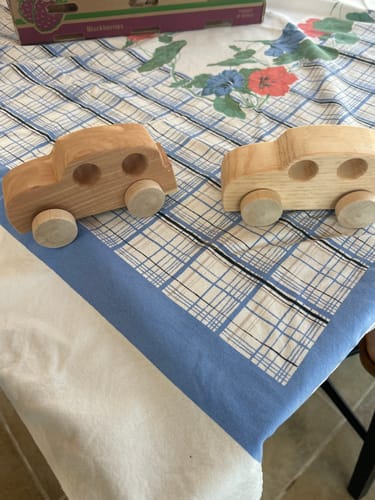 Customer's photo of two smooth, handmade wooden toy cars displayed on a checkered tablecloth.
