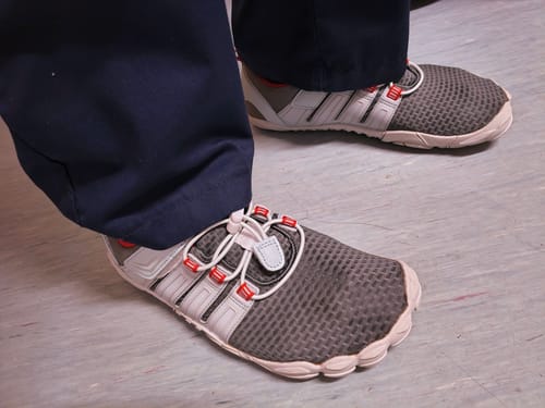 Customer wearing the grey Vigor II Barefoot Shoes with dark trousers, showing the fit in a work setting.