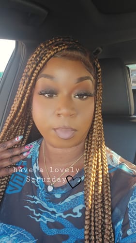 A reviewer wearing a long, honey-blonde braided wig, showing the natural-looking hairline.