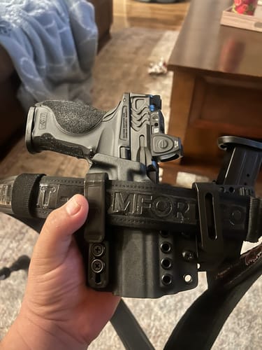 Customer holding a custom black holster for a pistol, attached to a thick belt in a home setting.
