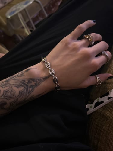 A reviewer wearing the silver Infinity Link Bracelet on their tattooed wrist, paired with several rings.