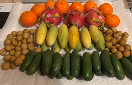 Ein Kunde zeigt die bestellten grünen Cocktailavocados, die zusammen mit anderen frischen Früchten aufgereiht sind.