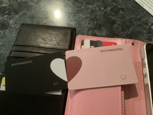 Customer shows black and pink SPOTMINDERS. Wireless Charger cards inside two different wallets on a table.