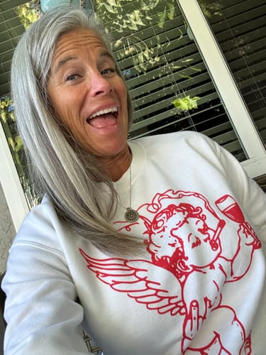 A happy reviewer wears the white Cupid Don't Care Sweatshirt, showing the red cherub graphic.