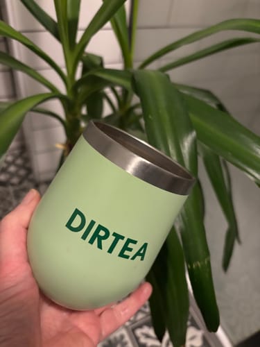 Reviewer's hand holding a light green insulated cup with the DIRTEA logo printed on it in dark green.