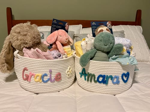 Customer's two personalized knitted baskets with names 'Gracie' and 'Amara' sitting side-by-side and filled with baby gifts.